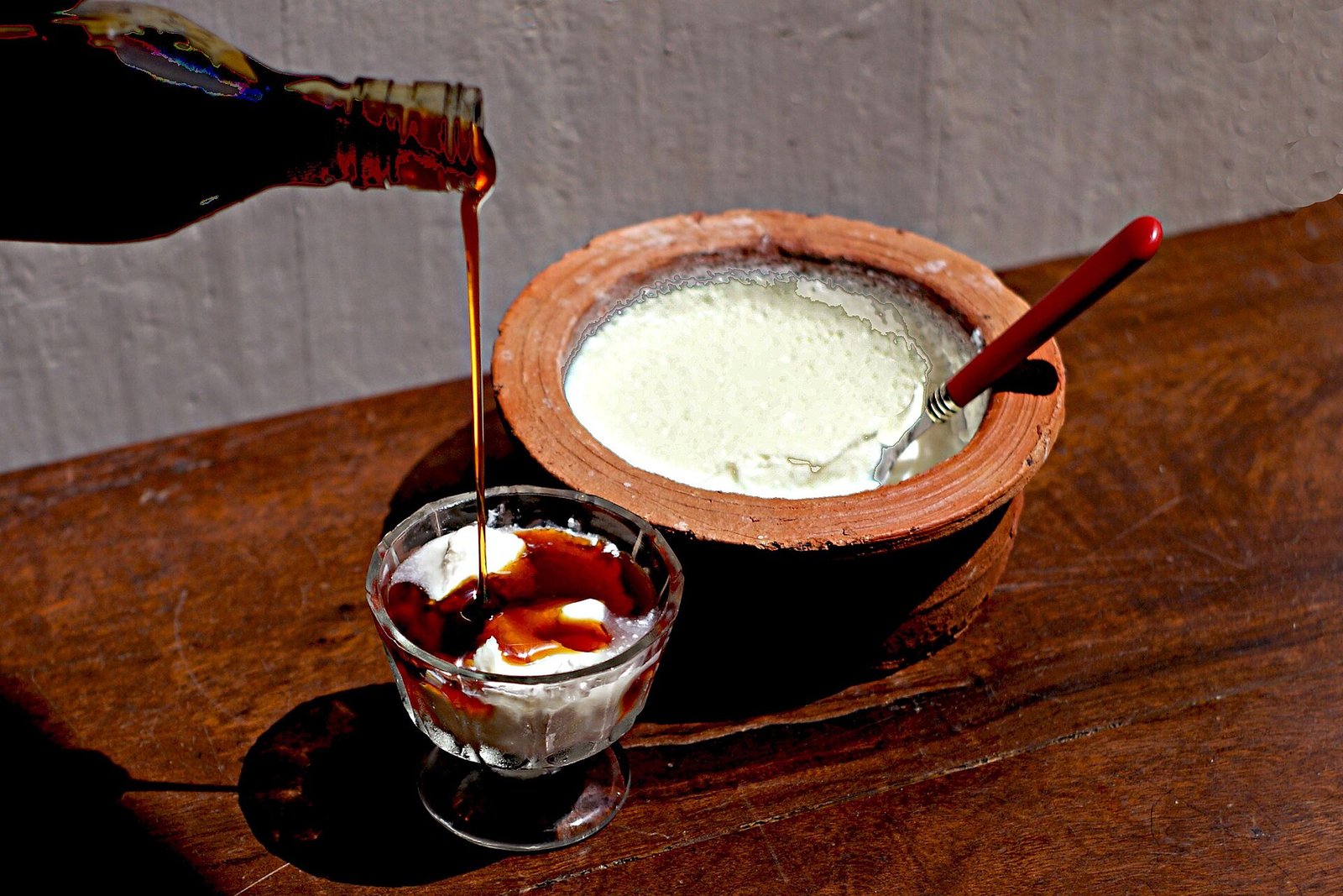 Kithul treacle being poured over buffalo curd in a clay pot