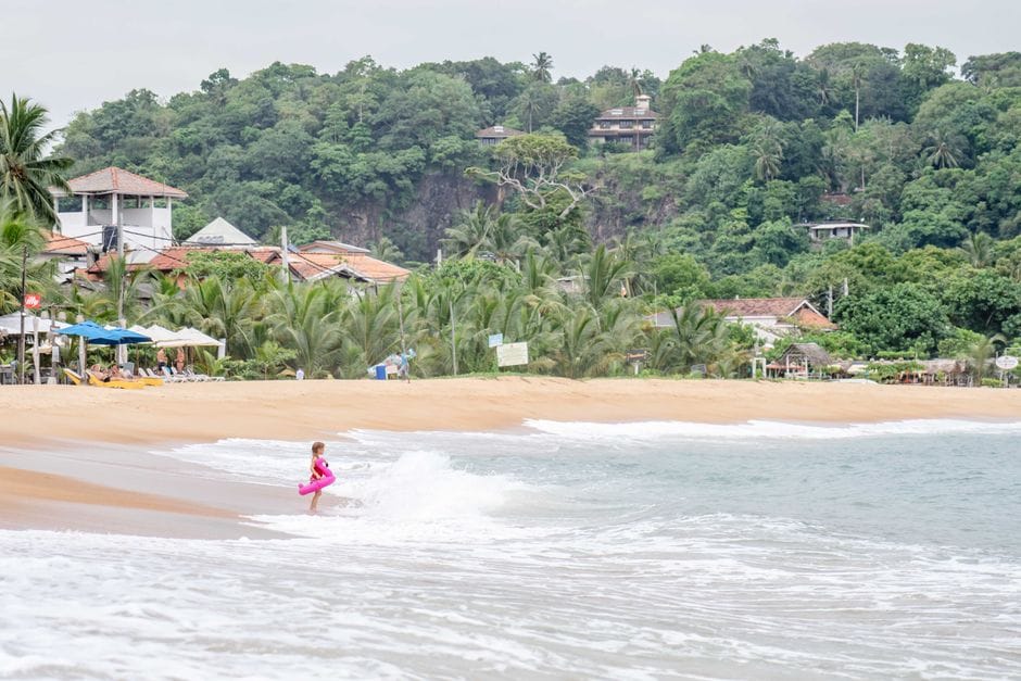 A child plays in the ocean waves at a serene tropical beach in Sri Lanka.