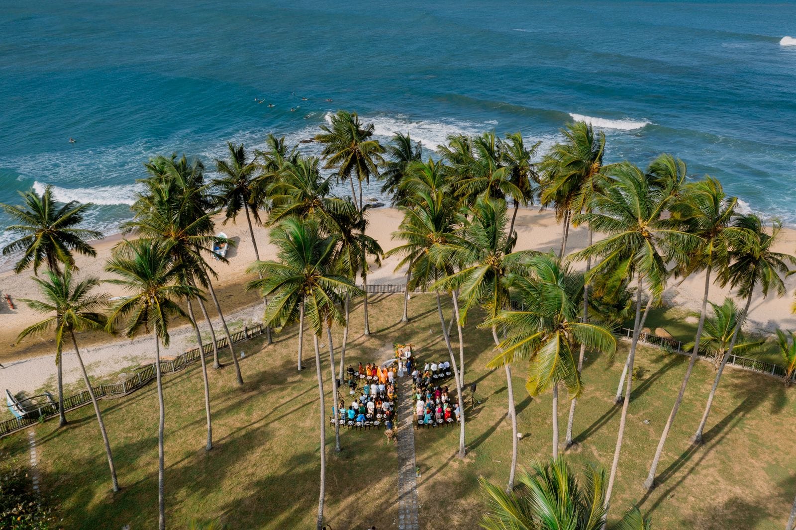 Palm trees and a ceremony on the beach at Arugam Bay seen from above