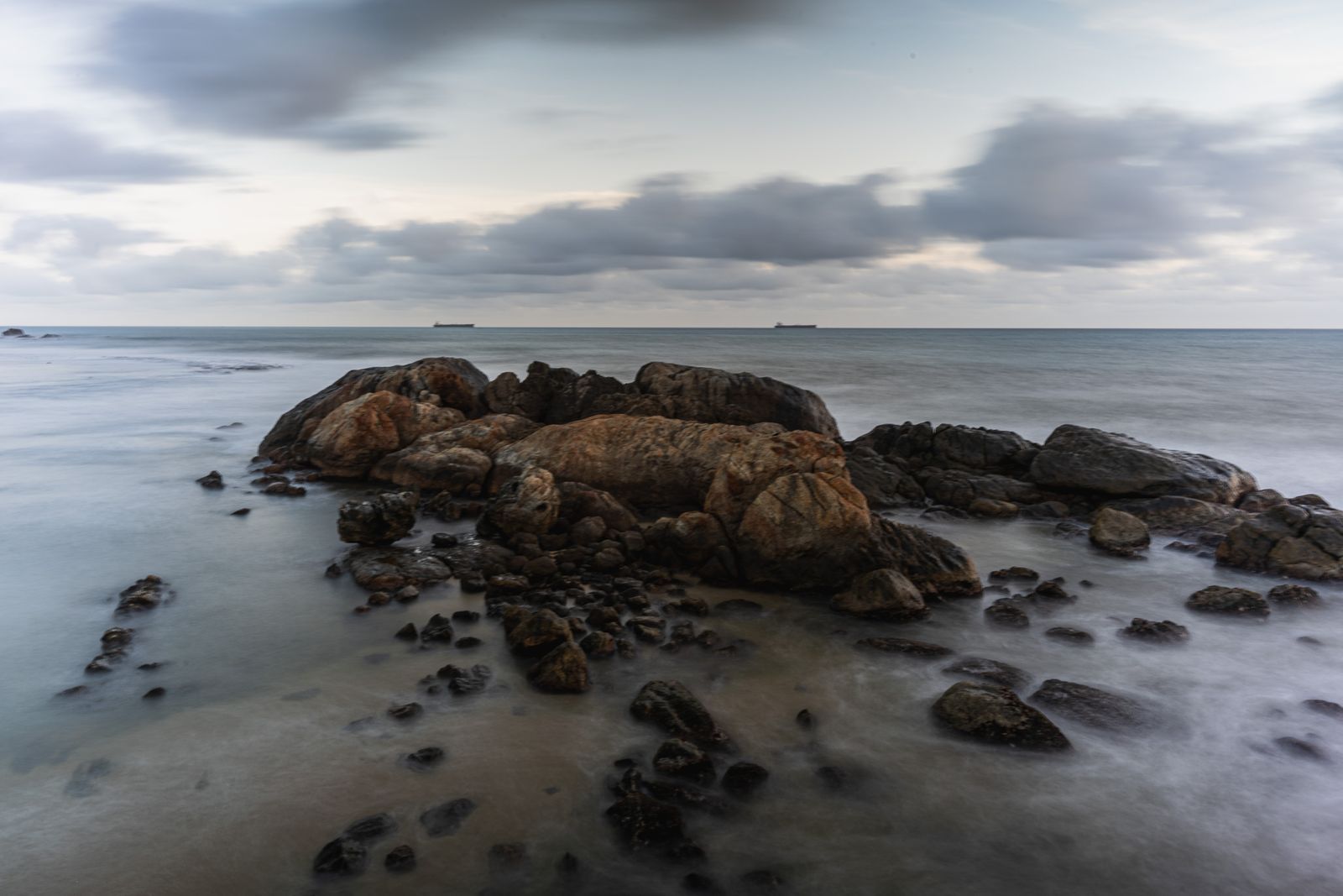 Serene rocky shoreline of Galle, Sri Lanka during twilight, with tranquil ocean waves and distant ships.