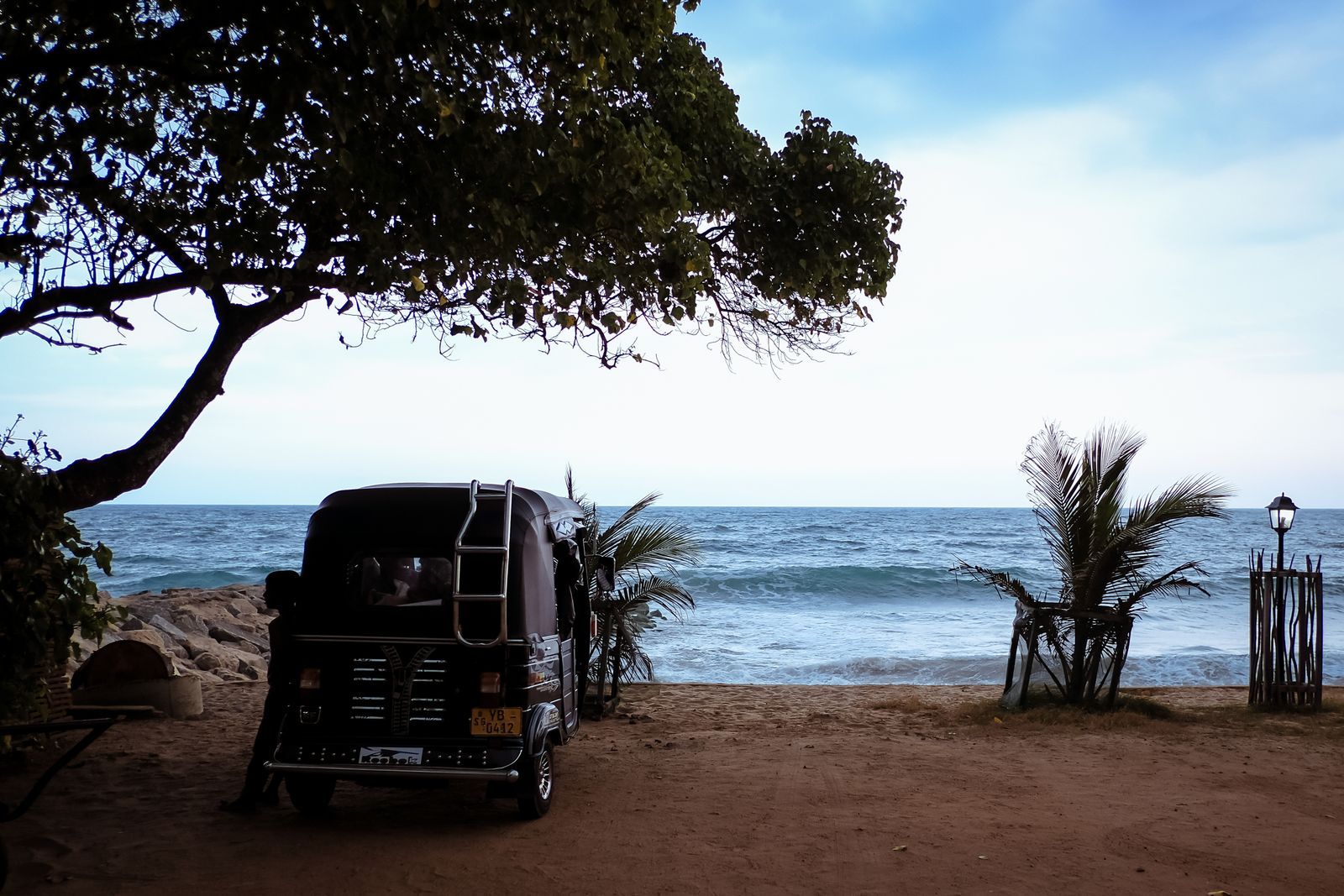 A tuk-tuk parked on a sandy beach in Sri Lanka overlooking the ocean